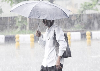 New Delhi: A man shields himself with an umbrella as heavy rains lash Delhi, on July 22, 2018. (Photo: IANS)